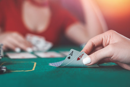 beautiful young girl sits at a poker table with cards in her hands and a player opposite. poker game of chance. woman's hands hold poker cards.の写真素材
