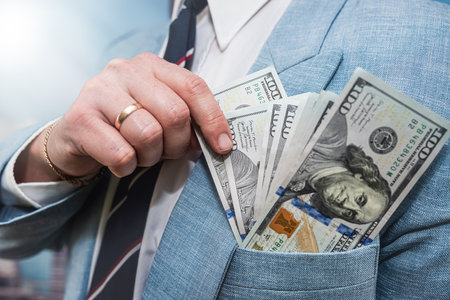 Businessman wear suit receive bribe and putting dollars money in pocket, corruption conceptの写真素材