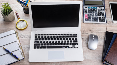 Laptop, blank notepad, pen calculator, reminder flower on office table. Top view. Distance office