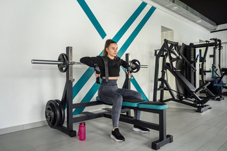 beautiful young sportswoman is exercising with a cable crossover exerciser in a fitness hall. the...