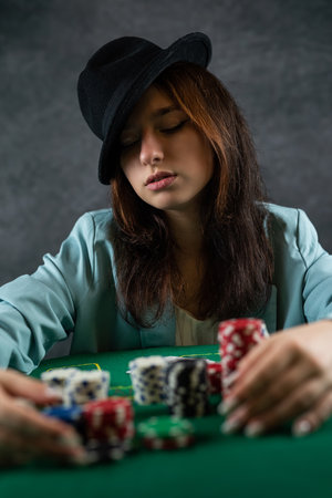 beautiful girl came to the night casino to play poker at a wide green table. a woman in a hat. poker game excitement. big moneyの写真素材