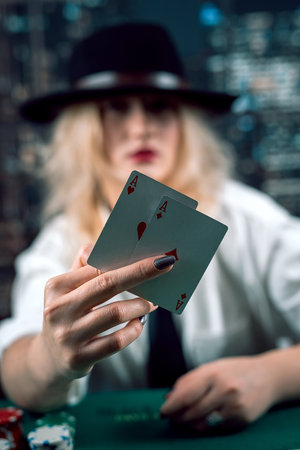 attractive girl in shirt and hat playing poker and holding cards in casino. woman player.poker. excitementの写真素材