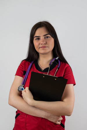 young female nurse wearing red uniform with stethoscope hold clipboard isolated on white background. Medical conceptの写真素材
