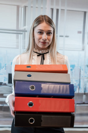 Attractive caucasian woman standing alone at the office and hold folder for paper documents
