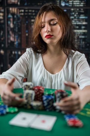 Young woman sitting at the table playing poker and holding chips smiling happy and positive. playing poker. a woman plays pokerの写真素材