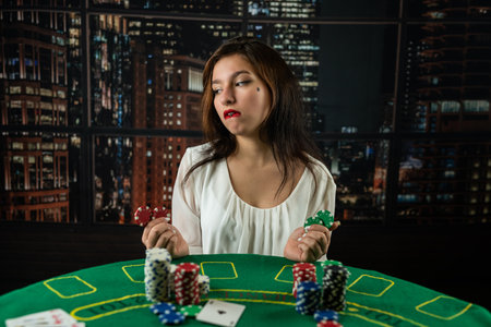 Young woman sitting at the table playing poker and holding chips smiling happy and positive. playing poker. a woman plays pokerの写真素材