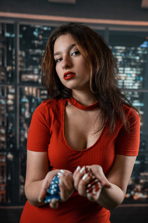 girl in a red dress showing a handful of multi colored poker chips posing. Poker. casino. Up closeの写真素材