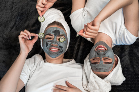 Two female friends lying on the floor together with facial masks and slice cucumbers for the freshness of the skin around the eyes. Skincare or natural care, beauty treatmentの写真素材