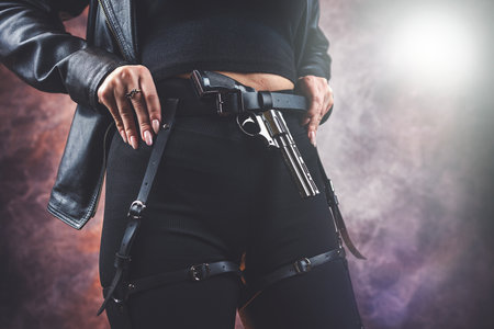 dangerous slim woman in black outfit holding handgun pistol isolated on dark, crime conceptの写真素材