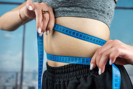 Attractive female trainer holds measuring tape for body measurement. isolated on a typical...