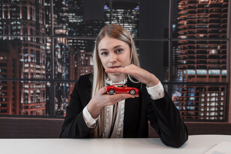 Small red toy car in the hands of business woman at office. Concept of car insurance. Rent or purchase vehicleの写真素材