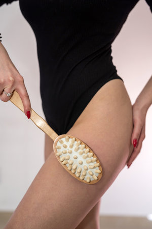 Young woman holding anti-cellulite massage dry brush near leg. Spa treatmentの写真素材