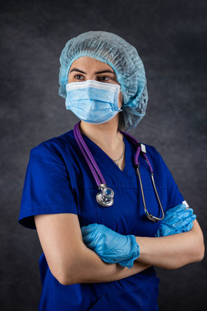 portrait of woman doctor or nurse wearing surgical mask and gloves with stethoscope isolated on dark. Woman hospital worker looking at camera, healthcareの写真素材