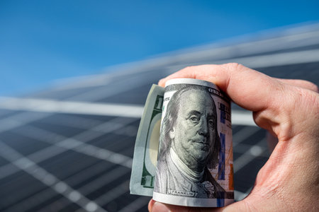 hand of a young man holding dollars to pay for the installation of new solar panels. Concept of...