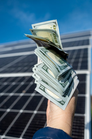 female hands with dollar bills on the background of solar panels. concept of green electricity. saving. saving electricityの写真素材