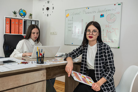 Two young business woman discussing financial charts as brainstorm meeting at office. Cooperate...