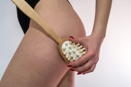 Young woman holding anti-cellulite massage dry brush near leg. Spa treatmentの写真素材