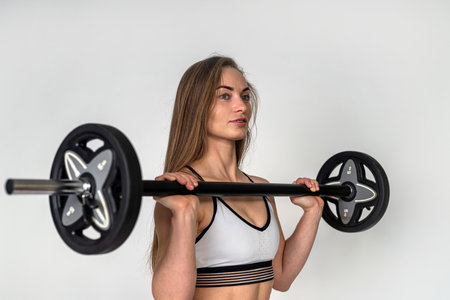 woman with a barbell in her hands flexing her muscles and doing a lunge in the gym against a white wall background. isolated sport as medicine. the beauty of the female bodyの写真素材