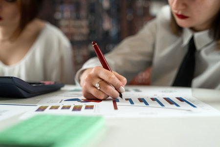 Two young business women working together with buisness graph at ofiice, paperwork conceptの写真素材