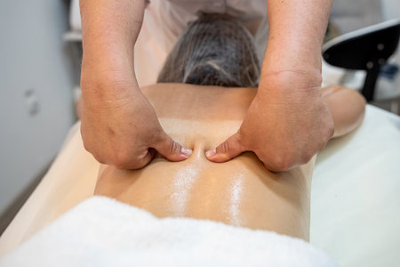 masseuse massages the back of a female client on a massage table close-up. spa salon concept. healthy bodyの写真素材
