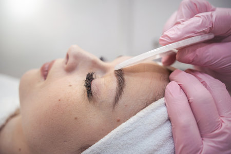 cosmetologist doing medical procedure with white gouache scraper on a client's face. Health lifestyleの写真素材