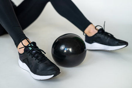 female beautiful legs in leggings and sneakers next to black fitness ball isolated on white floor. sport as life. sportswomanの写真素材