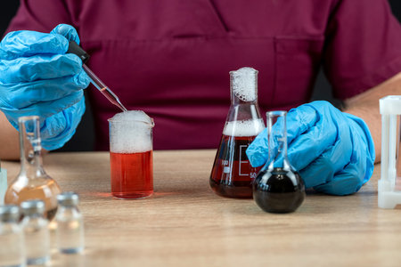 Professional scientist in red uniform and gloves mixing reagents with test tubes. Chemistry science laboratory flaskの写真素材