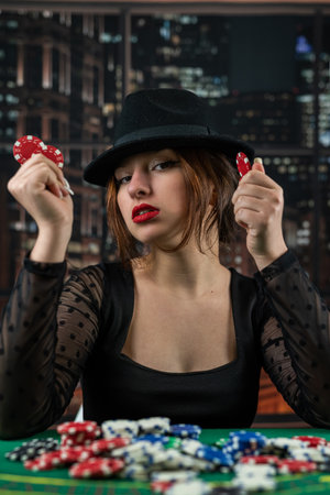 attractive girl in a black dress is leaning on the table, holding a poker chip and looking away. poker. casino. Gambling.の写真素材