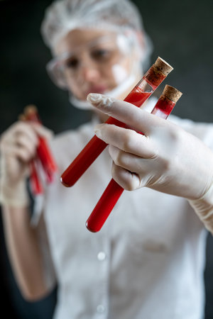 caucasian young doctor or biochemist in white coat looking a test tube with blood sample isolated on black.の写真素材