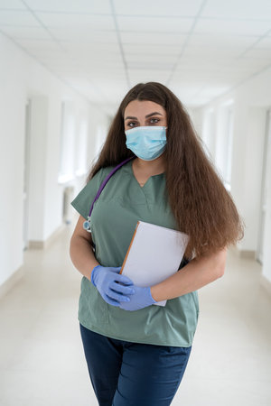 Portrait of caucasian attractive female nurse ot sudent wear uniform and stethoscope at clinic corridor. Medical staffの写真素材