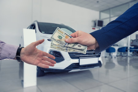Car salesman and buyer finish deal to but new car at auto showroom. Modern beautiful showroom with cars being soldの写真素材