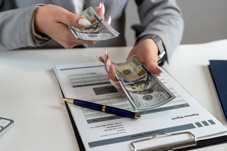 Female accountant count dollar paper money for payment salary and income at modern office, laptop...