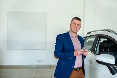 young salesman in suit waiting for customer at the dealership. purchase car concept. transportationの写真素材