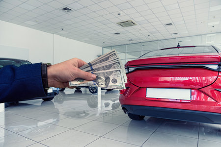 Man with 100 dollar banknotes to buy a new car at the dealer showroom. New car is a new dream.
