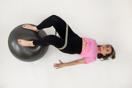 sporty attractive woman doing stretching exercising with fit ball and rubber band isolated on white. Works on musclesの写真素材