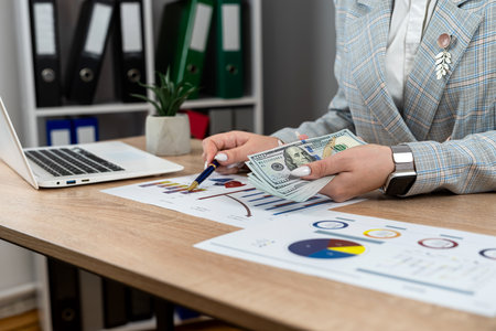 Female accountant count dollar paper money for payment salary and income at modern office, laptop and business graph and chart. Financial conceptの写真素材
