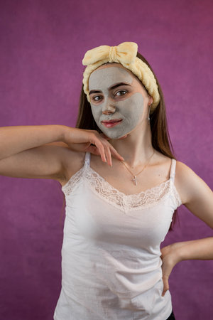Beautiful woman with therapeutic green clay facial mask isolated on purple. Spa anti aging treatmentの写真素材
