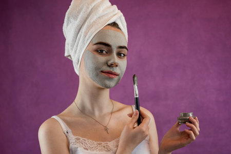 Portrait of young woman with green clay mask on her face isolated on violet. Beauty treatments, perfect cleanの写真素材