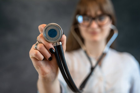attractive female nurse or intern in white medical uniform with stethoscope, isolated on dark. Welcome in clinic, healthcare workerの写真素材