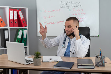 Portrait of man doctor therapist practitioner in white coat and stethoscope working at desk alone in modern clinic. Distance medicine conceptの写真素材
