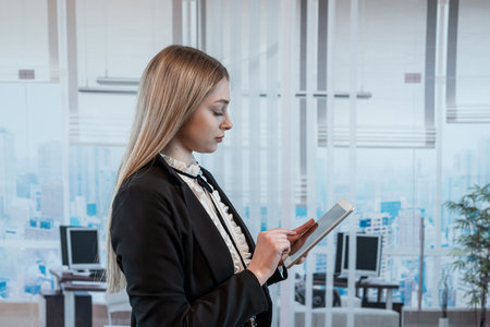 Young caucasian business woman in black suit checks email on smartphone cellphone at office. Lifestyleの写真素材