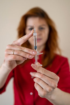 Portrait of woman doctor in red unifrom and gloves holding syringe with vaccine isolated, healthcare...