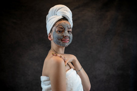 Beautiful young woman wear white towel applying gray oxygen bubbling mask isolated on black, anti aging treatment, perfect skinの写真素材