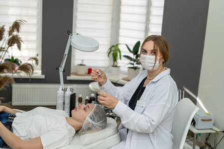 cosmetologist holds a pipette with essential oil on face of patient girl. Concept of aromatherapy and massage to the patient at spaの写真素材