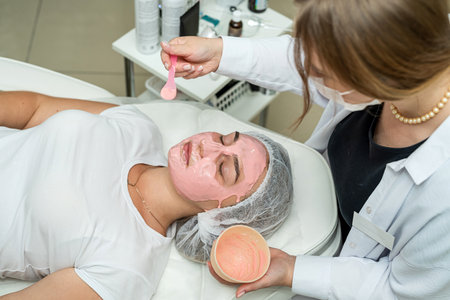 pretty caucasian woman having a pink clay facial mask at beauty salon. Concept of spa treatmentの写真素材