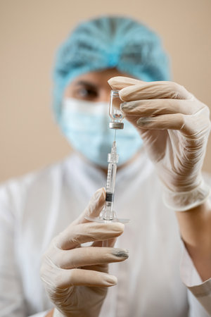 caucasian female doctor in a medical uniform and protective mask and hold syringe with vaccine. covid-19 vaccinationの写真素材
