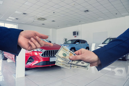 man gives dollar cash to dealer man when buying a car at modern showroom. Deal of buy or rent new autoの写真素材