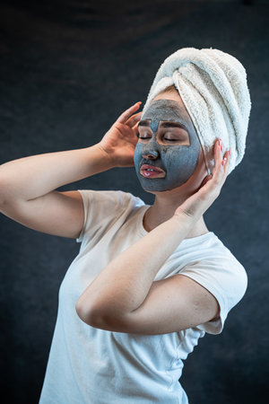 Portrait of attractive young woman apply clay mud mask on her face isolated on black. Peeling mask on facial skin, body care. Anti aging treatment at homeの写真素材
