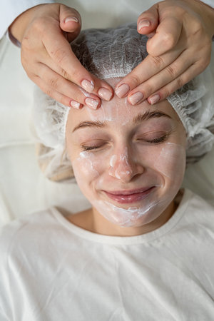 Beautiful young girl receive nourishing cream on here face, spa procedures. Concept of cleaning and facial skin careの写真素材