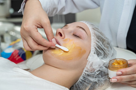 cosmetologist applying gold facial mask by brush on face female client at spa. Healthcare conceptの写真素材